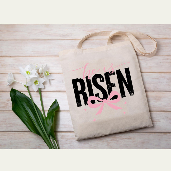 Ready-to-press DTF transfer with "He Is Risen" text in bold black letters and a pink bow design.