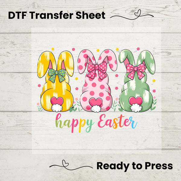 Three colorful bunnies with bows, fluffy tails, and rainbow "Happy Easter" text, perfect for festive apparel.