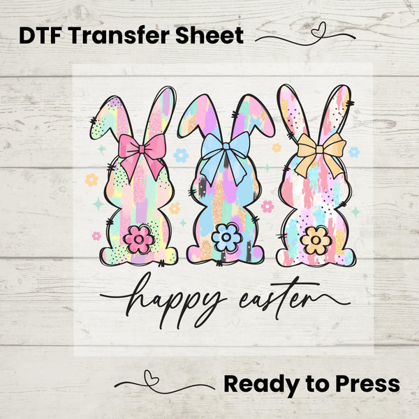 Three watercolor-style pastel bunnies with bows and flowers, featuring a "Happy Easter" script for festive apparel.