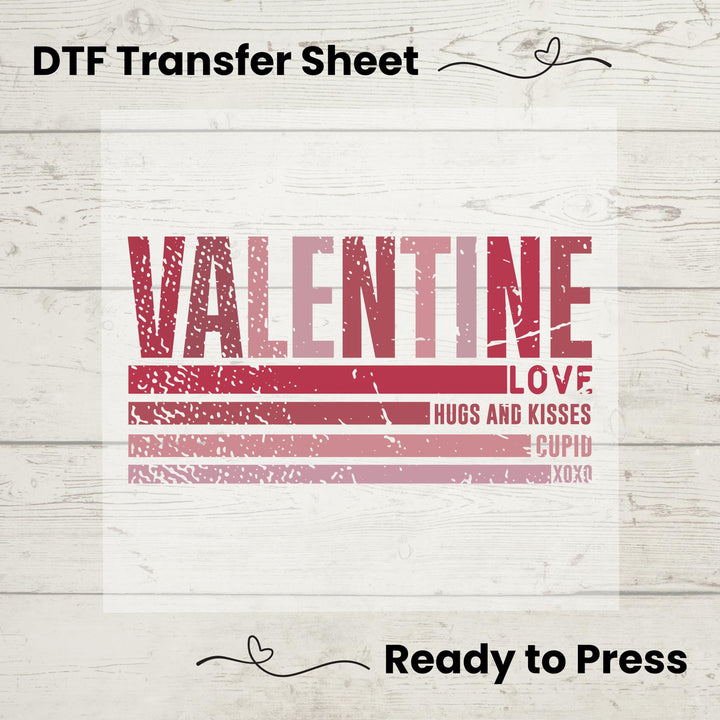 A DTF transfer sheet with the text 'VALENTINE LOVE HUGS AND KISSES' on a wooden background, indicating it's ready to be pressed onto fabric.