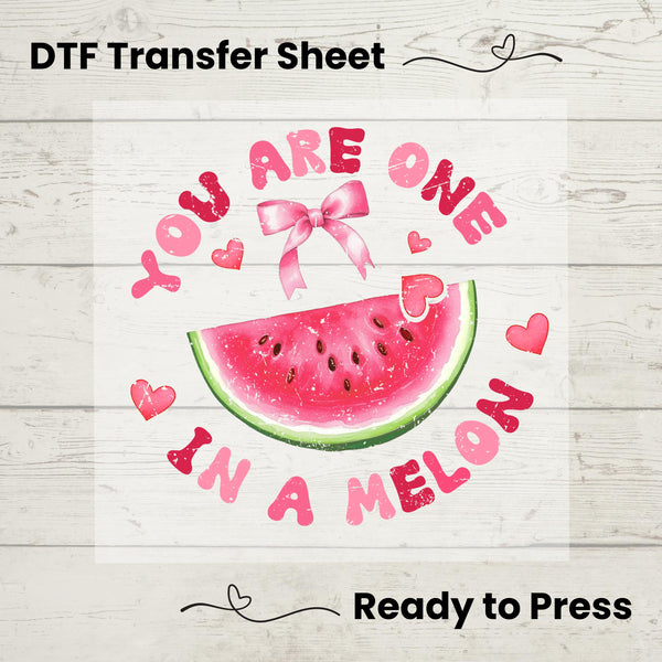 A graphic design of a watermelon slice with the text 'YOU ARE ONE IN A MELON' surrounded by heart shapes, indicating a Valentine's theme. The words are stylized in a playful, romantic font, with the entire design presented on a wooden planked background, indicating a ready-to-press DTF (Direct to Film) transfer sheet.