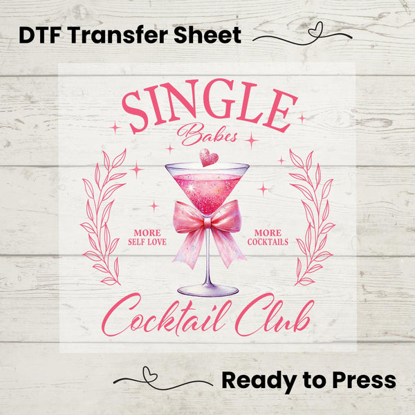 A digital image of a DTF transfer sheet with the text 'Single Babes Cocktail Club' and a graphic of a pink martini glass, indicating it's ready to be pressed onto fabric.