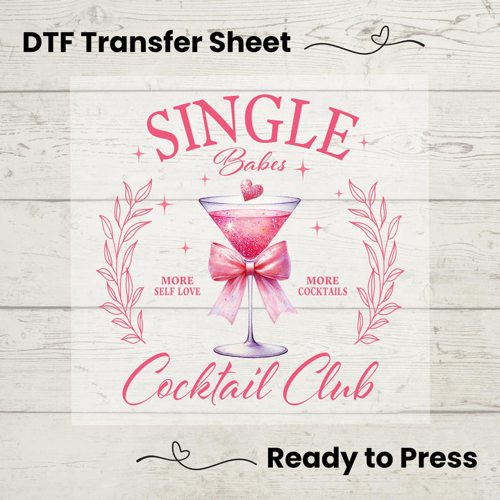 A digital image of a DTF transfer sheet with the text 'Single Babes Cocktail Club' and a graphic of a pink martini glass, indicating it's ready to be pressed onto fabric.
